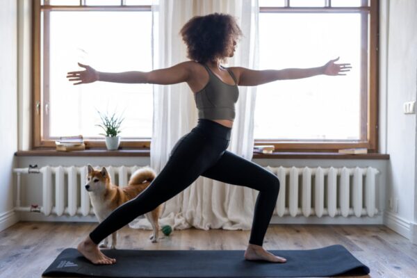 A woman doing yoga on a mat with her dog in a cozy home setting.